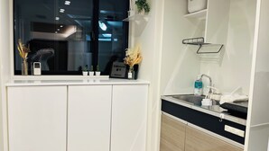 Een moderne keuken met witte kasten, een zwart aanrecht en een raam boven de gootsteen. Op de vensterbank staan kleine potplantjes en er staat een welkomstbord.