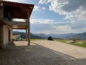 Ein überdachter Außenbereich mit Steinboden, einer Holzpergola und Blick auf ferne Hügel.