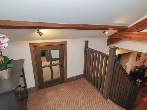 A wooden staircase with a carpeted landing, a door with a glass panel, and a potted orchid. - The Opulent (Hexham)