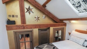A bedroom with a sloped ceiling, wooden beams, a bed with patterned bedding, and a door with a window. - The Opulent (Hexham)
