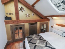 A bedroom with a sloped ceiling, wooden beams, a bed with patterned bedding, and a door with a window.