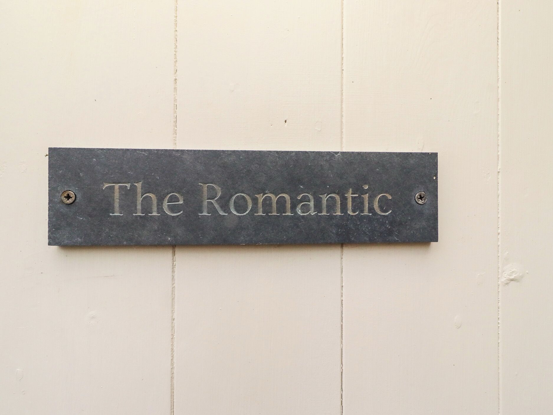 Eine Metallplakette mit der Aufschrift "The Romantic" an einer weißen Wand.