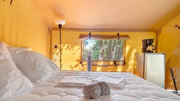 A bed with a white quilt, a rolled towel, and a coffee maker on a small table.