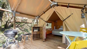 Un espacio al aire libre con carpa, una parrilla, una mesa pequeña y una cama.