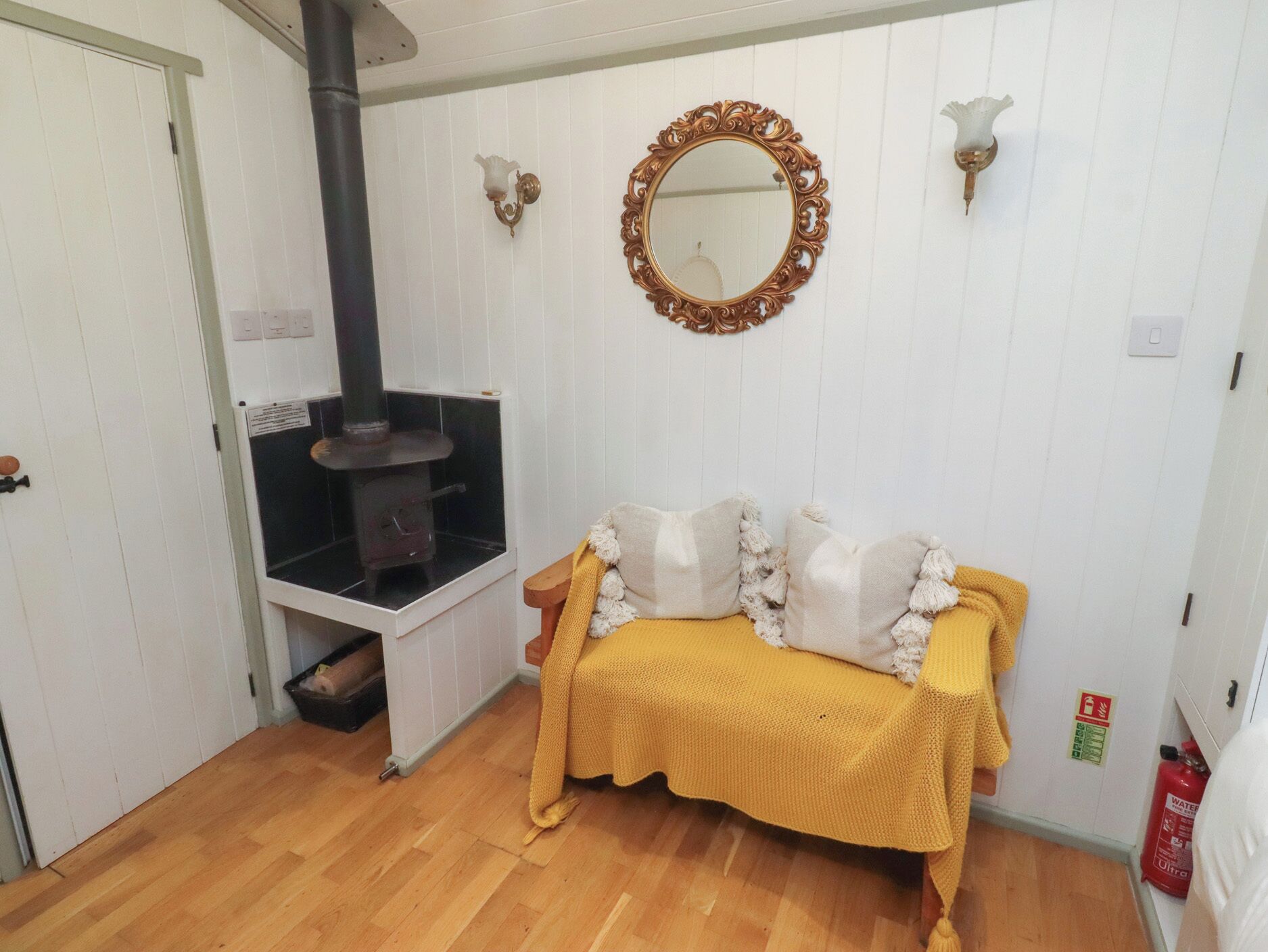 A cozy room with a wooden floor, a sofa with a yellow blanket, a fireplace, and a decorative mirror.