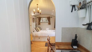 A narrow hallway leading to a bedroom with a bed, a wooden chair, a table, and a kitchen area with a sink and utensils. - Woodland (Hexham)