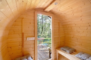 Una cabaña de madera con cama de altillo, un banco y una mesa con sillas afuera.