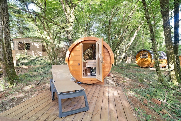 Een houten hutje met een ronde deur, een bankje en een kleine tafel, gelegen in een bos.
