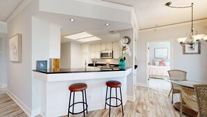 Una cocina moderna con armarios blancos, una isla central con taburetes, un microondas y un reloj decorativo.