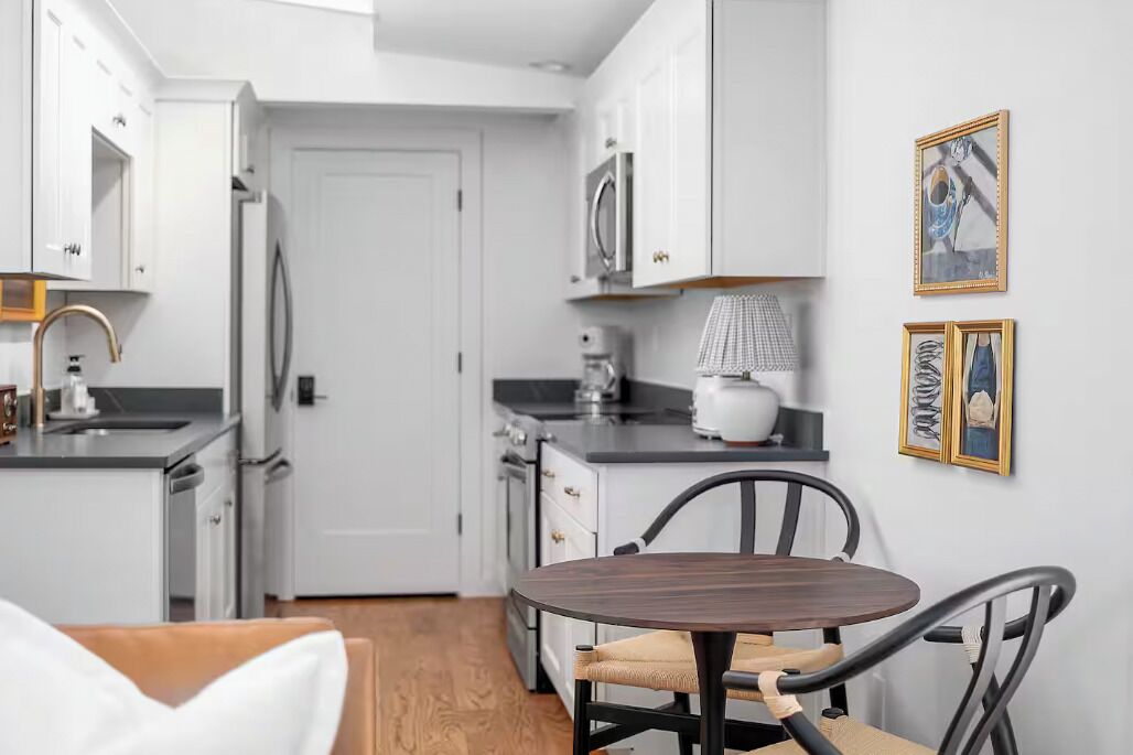 A modern kitchen with white cabinets, a microwave, a coffee maker, and a dining table with chairs.