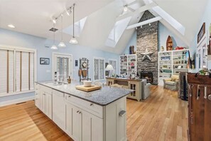 A spacious kitchen with a large island, a stone fireplace, and a lofted ceiling with skylights.