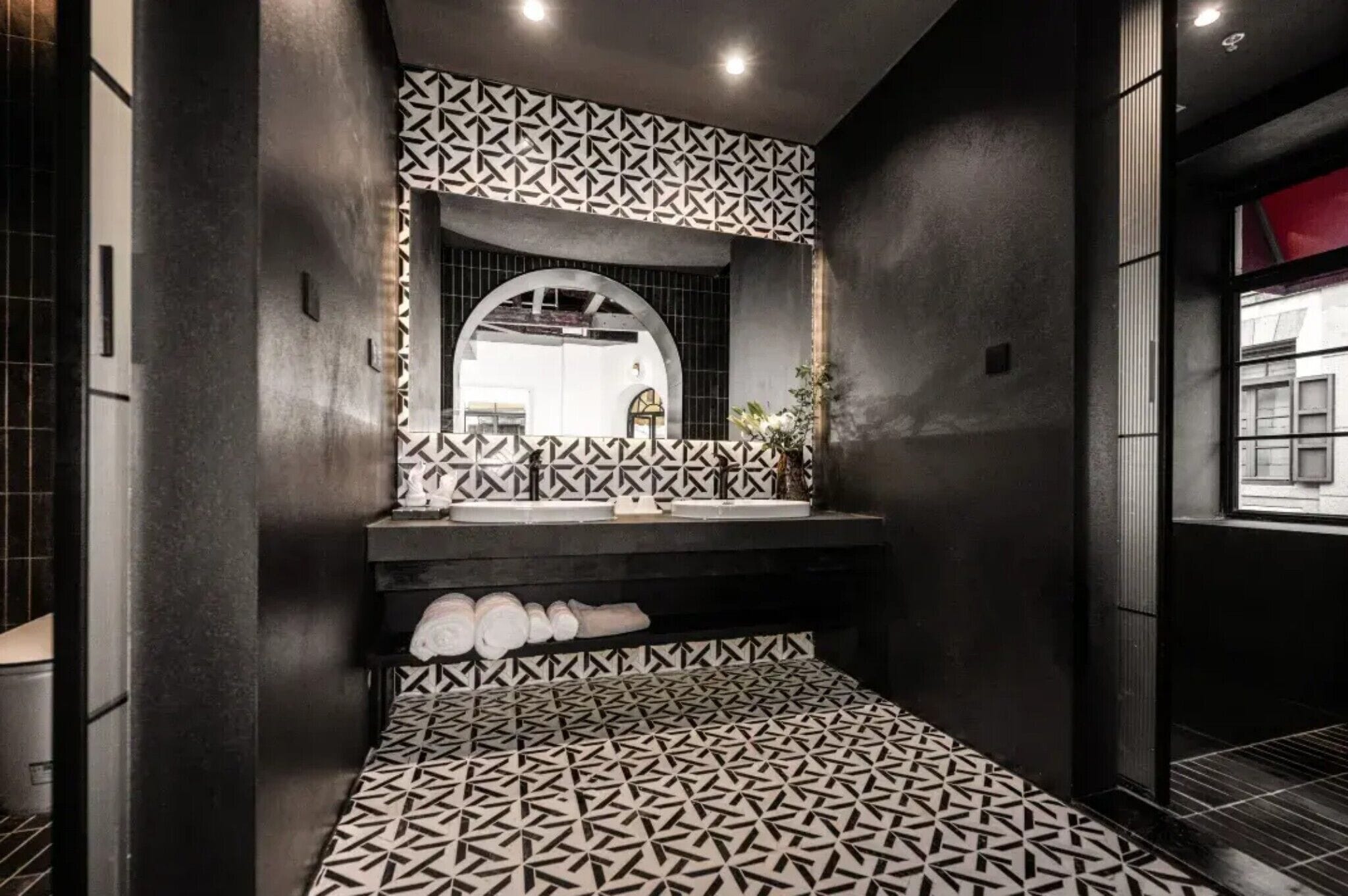 A modern bathroom with a geometric patterned floor, a large mirror, and a dark wall with a geometric pattern.
