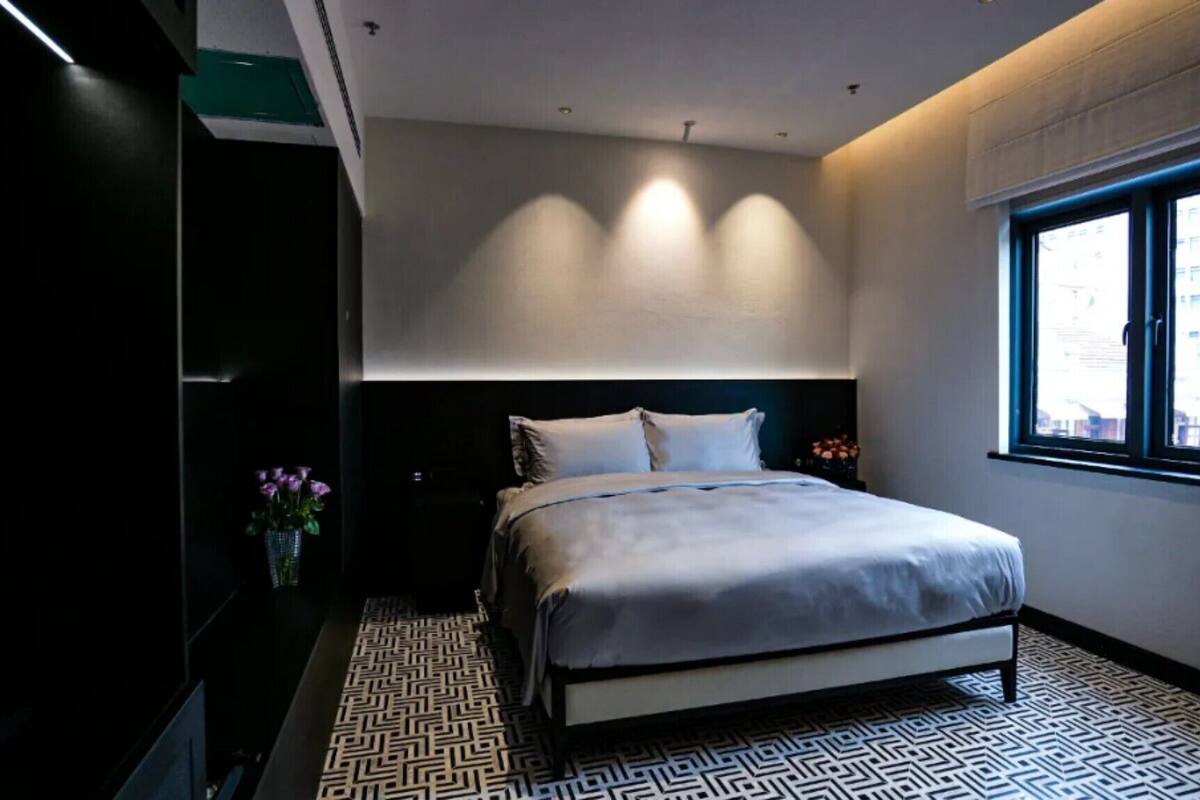 Un dormitorio moderno con una cama grande, una mesita de noche, un jarrón con flores y una ventana con vista a la ciudad.