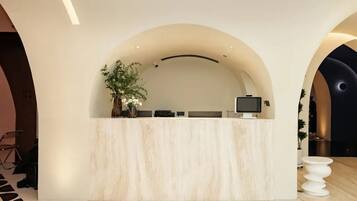 A reception desk with a curved arch, a potted plant, and a flat-screen TV.
