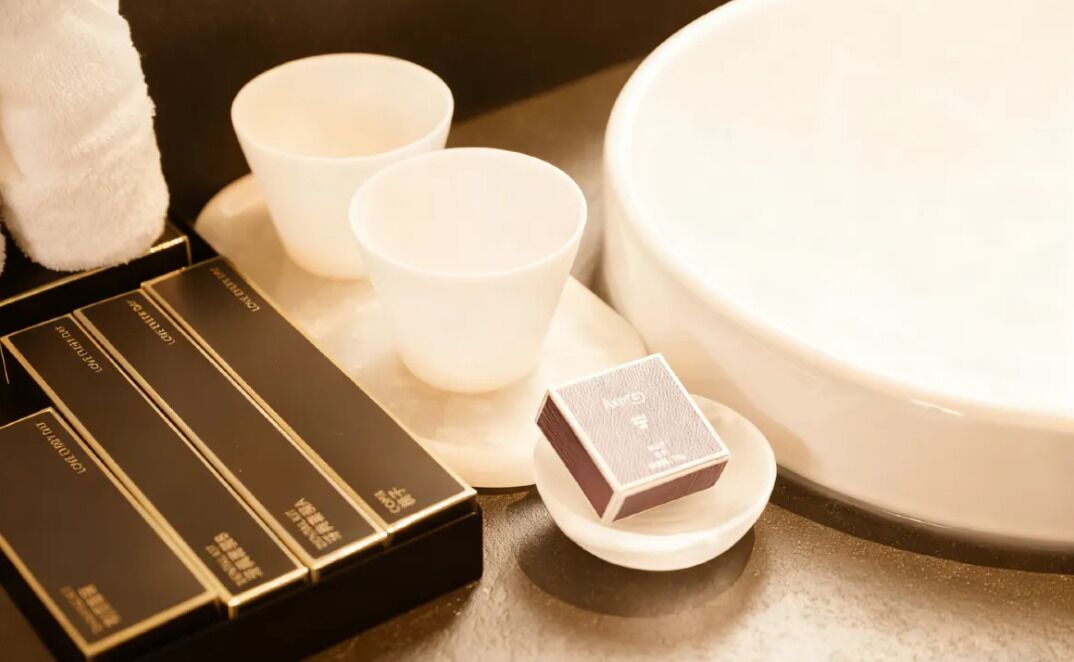 Un ensemble de tasses et de soucoupes blanches, disposé sur un plateau, une serviette blanche et une petite boîte de thé, le tout posé sur une table.