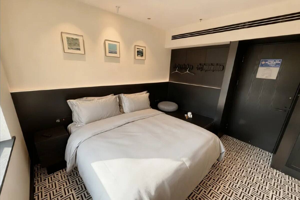Habitación de hotel con una cama grande, cabecera con motivos artísticos, mesita de noche pequeña y piso con diseño.