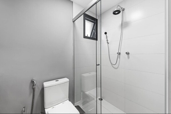 A modern bathroom with a glass shower enclosure, a toilet, and a visible showerhead. - Soma Perdizes 1101 (São Paulo)