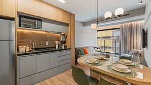 Une cuisine moderne dotée d’appareils électroménagers intégrés, un coin repas avec une table ronde et une vue sur la ville grâce à de grandes fenêtres.