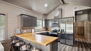Une cuisine moderne avec un îlot central en bois, des appareils électroménagers en acier inoxydable et des tabourets de bar.