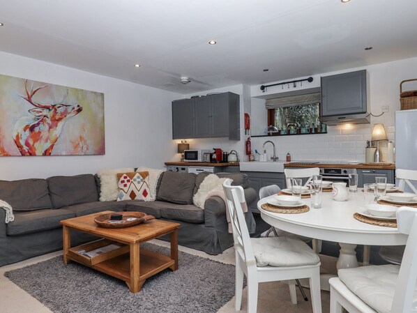 A modern living room with a grey sofa, a wooden coffee table, and a dining area with white chairs and a round table. - Clifford Lodge Barn (Exeter)