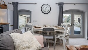 Une cuisine de taille réduite avec un coin repas, une horloge au mur et une vue à travers la porte.