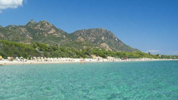 Ein Strand mit klarem türkisblauem Wasser und einer gebirgigen Kulisse.
