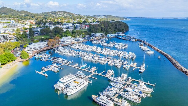 An aerial view of a marina with numerous boats docked, surrounded by residential buildings and greenery. - Bay Breeze Apartments, 33   1 Trafalgar St - Aircon, Wi-Fi, Linen, Pool (Nelson Bay)