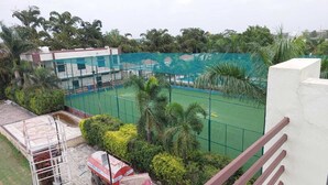 A sports court with a net, surrounded by greenery and a building with multiple windows. - utsav hotel and resorts (Burhanpur)