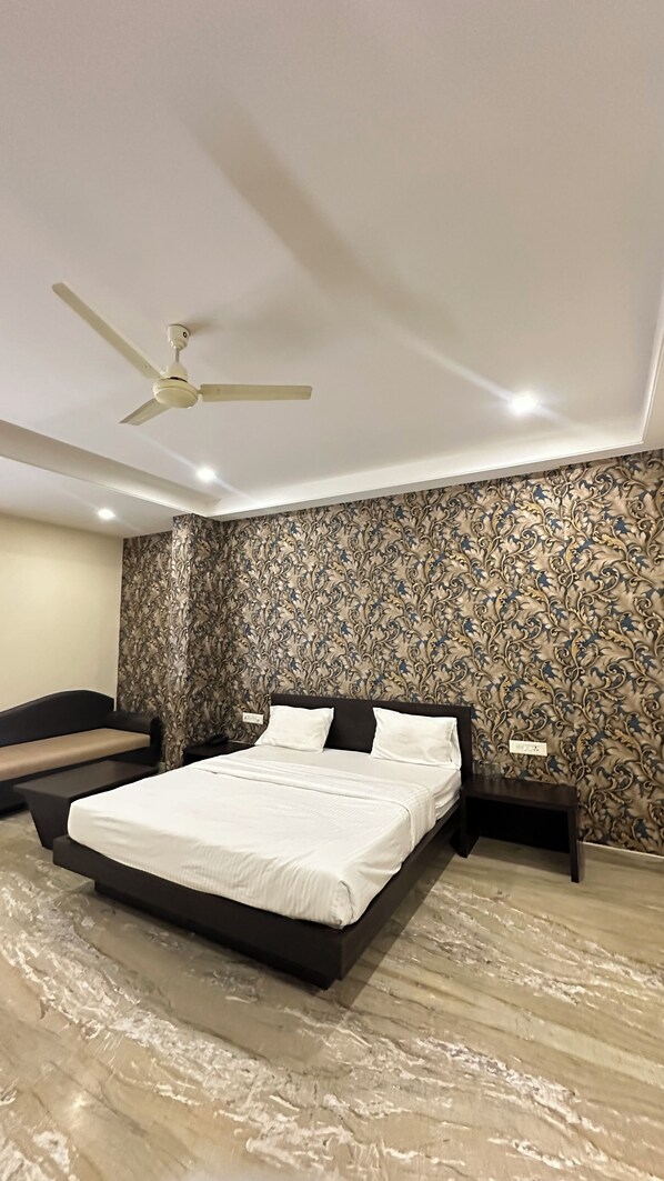 A bedroom with a bed, a nightstand, a ceiling fan, and patterned wallpaper. - utsav hotel and resorts (Burhanpur)