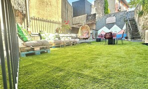 A backyard with a grassy lawn, a swing set, and a seating area with chairs and a table.