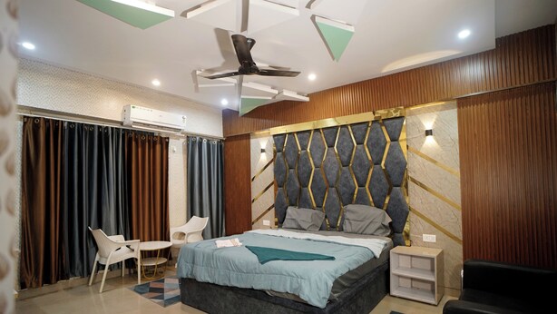 A modern bedroom with a bed, a ceiling fan, a nightstand, a chair, and a small table. - The Bless Code (Lucknow)
