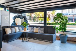 Ein modernes Interieur mit einem dunkelgrauen Sofa, gemusterten Kissen, einem kleinen runden Tisch und einem Topf mit Pflanze.