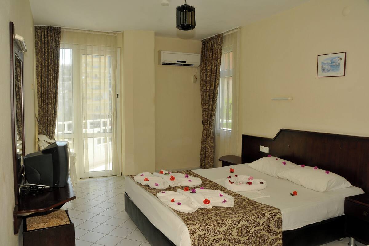 A hotel room with a bed, a television, an air conditioning unit, and a window with curtains.