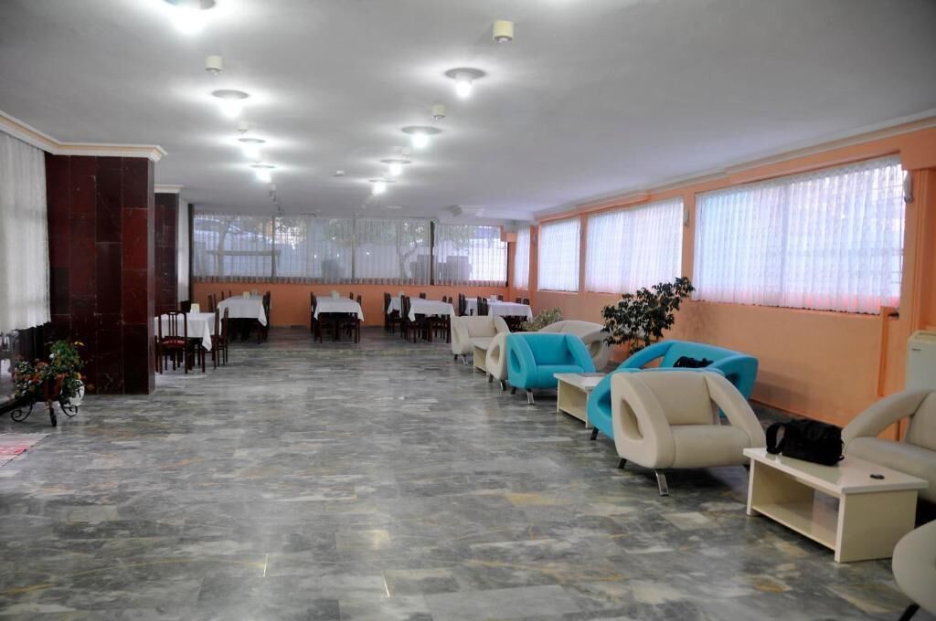 Un vestíbulo de hotel con suelo de mármol, zonas de estar con sofás y sillones, un mostrador de recepción y ventanas grandes con cortinas.