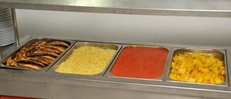 A buffet with grilled fish, shredded cheese, red sauce, and pineapple chunks.