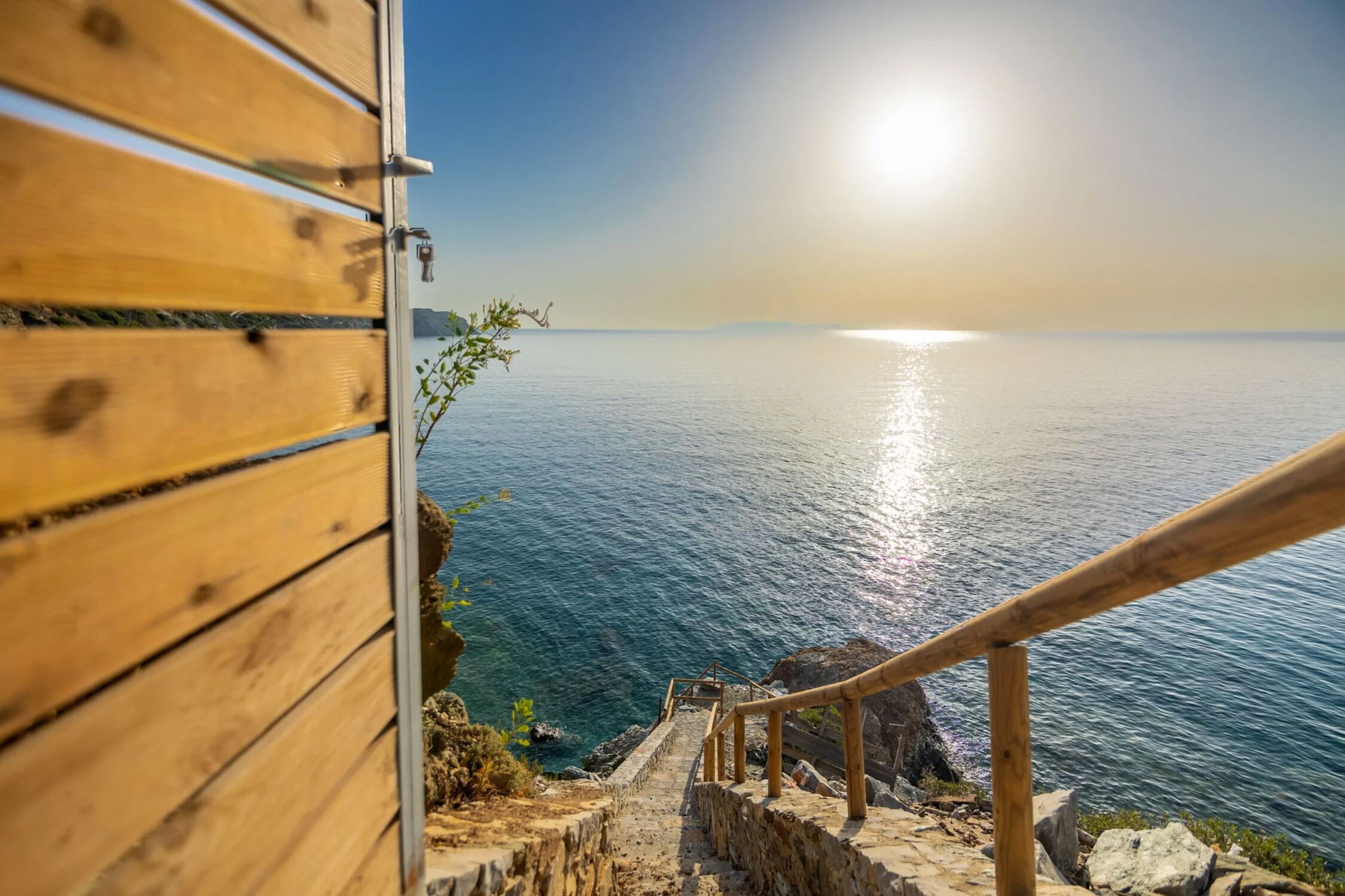 A wooden staircase leading to a coastal view with a clear sky.