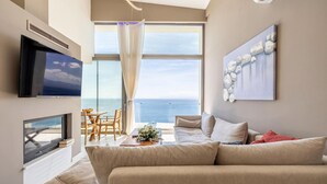 Una sala de estar moderna con un televisor grande, un sofá, una mesa de comedor y vistas al océano.