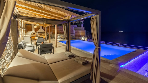 Un espacio lounge exterior moderno con piscina, asientos cómodos y una pérgola con iluminación cálida.