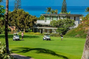 Ein Golfplatz mit Blick auf das Meer und ein modernes Gebäude im Hintergrund.