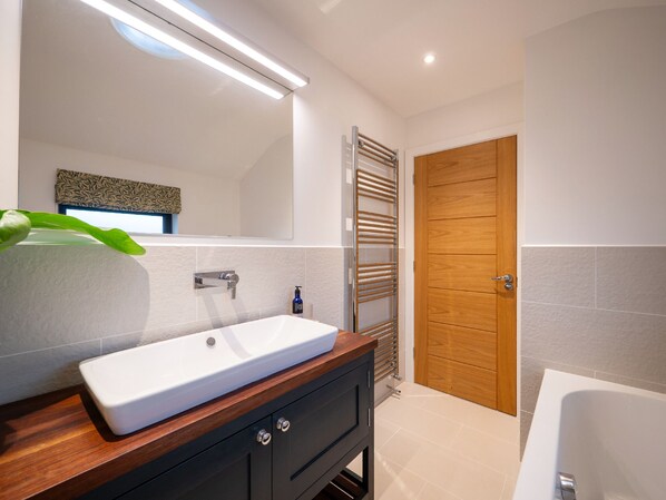 Un bany modern amb un lavabo blanc, un armari de tocador de fusta i un mirall gran.