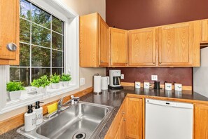 Una cocina moderna con armarios de madera, un lavamanos de acero inoxidable, una cafetera y un dispensador de jabón para lavar platos.