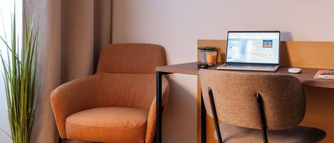 A modern room with a wooden desk, a laptop, a plant, and a comfortable chair.