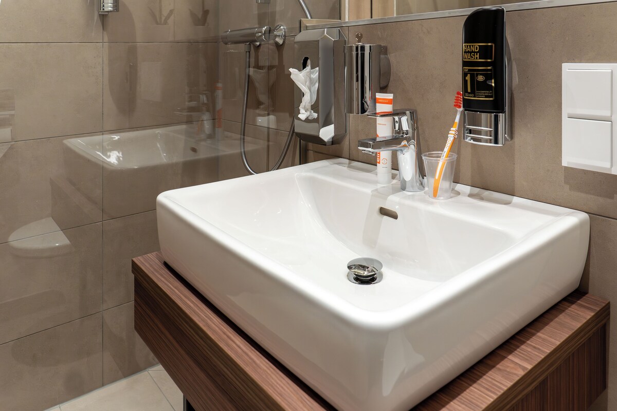 A modern bathroom with a white sink, a hand wash station, and a glass shower enclosure.