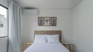 Ett hotellrum med en säng, två sängbord, ett fönster med gardiner och tre inramade tavlor på väggen.