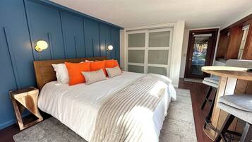A bedroom with a bed, bedside tables, a bench, a window with blinds, and a door leading outside.