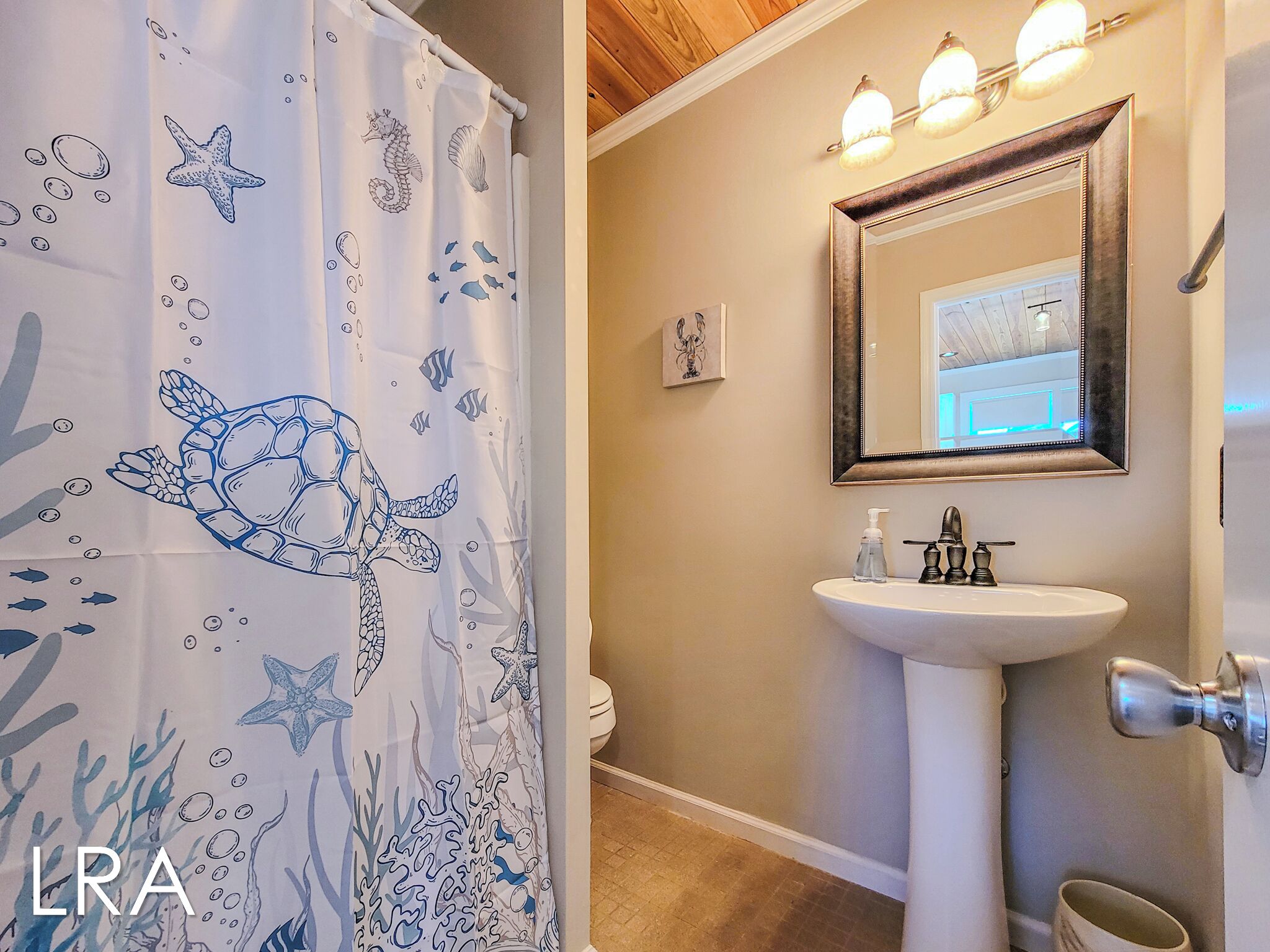 Un bagno con un lavandino bianco, uno specchio e una tenda da doccia con decorazioni di tartarughe marine e pesci.