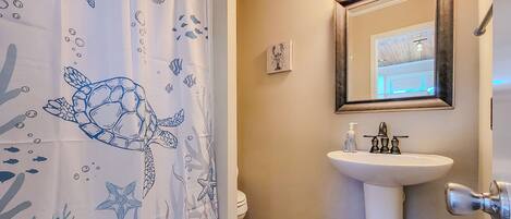 Un bagno con un lavandino bianco, uno specchio e una tenda da doccia con decorazioni di tartarughe marine e pesci.