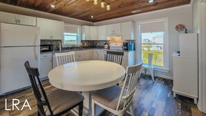 A modern kitchen with white cabinets, a round dining table, and a wooden ceiling. - Fins Up - NEW Beachside Escape (North Topsail Beach)