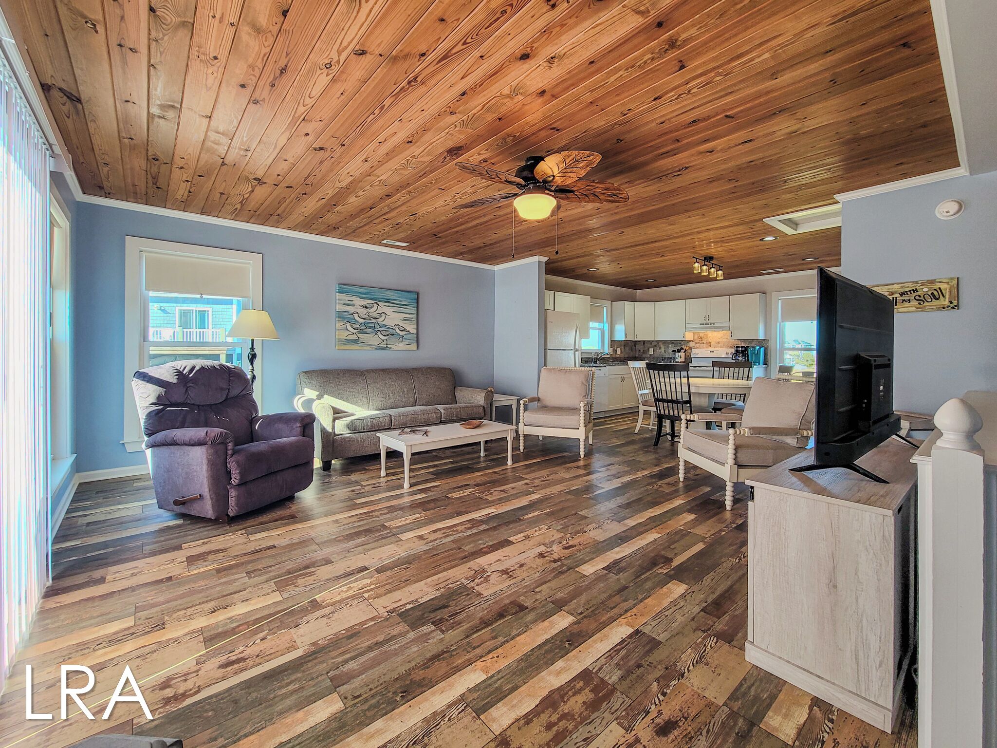A spacious living area with a wooden ceiling, a sofa, armchairs, a coffee table, and a television.