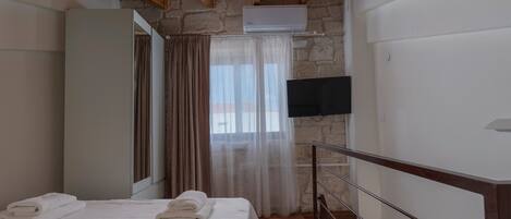 A bedroom with a bed, a TV, a window with curtains, and a stone wall.